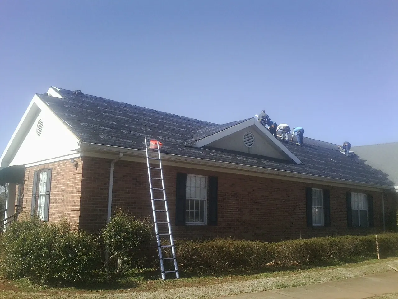 Crew tearing shingles off a brick ranch roof with a ladder set — Metal Roof Repair work by our crew in Sidney